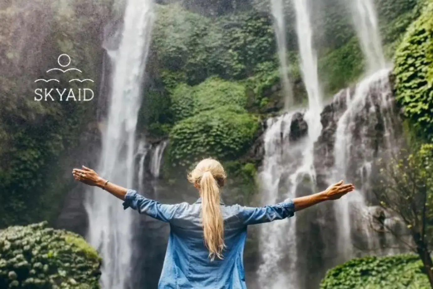 mujer con los brazos abiertos frente a una cascada, conectando con la paz interior a través de la gratitud