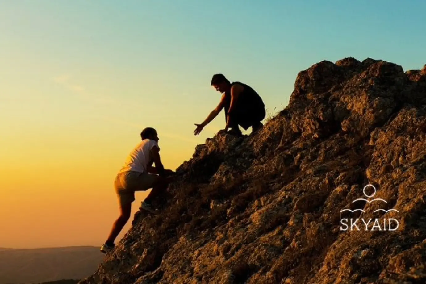 Dos personas ayudándose a escalar una montaña al atardecer, reflejo de la realidad y propósito espiritual compartido